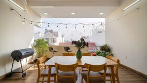 Een dakterras met een eettafel, stoelen, een barbecue en lichtjes.