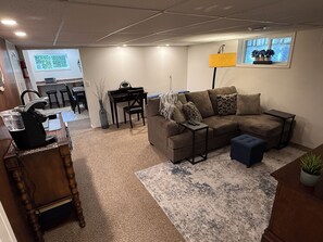 A living room with a sectional sofa, a coffee table, a desk with a chair, a lamp, and a television. - Cozy 2 bedroom suite in downtown Kelowna BC (Kelowna)