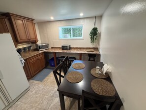 A compact kitchen with wooden cabinets, a microwave, a toaster, and a dining table with woven placemats. - Cozy 2 bedroom suite in downtown Kelowna BC (Kelowna)