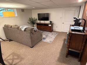 A living room with a sofa, a television, a wooden cabinet, and a desk with a computer. - Cozy 2 bedroom suite in downtown Kelowna BC (Kelowna)