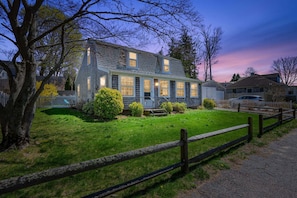 A two-story house with a front porch, a garage, and a well-maintained lawn. - Cozy Getaway with Beach Pass & Sunroom (Osterville)