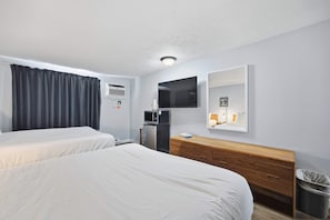 Camera d'albergo con due letti, una cassettiera in legno, una televisione, un piccolo frigorifero, un condizionatore d'aria e un cestino.