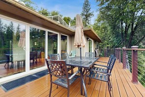 A deck with a table and chairs, a covered umbrella, and a glass door leading to an outdoor area.