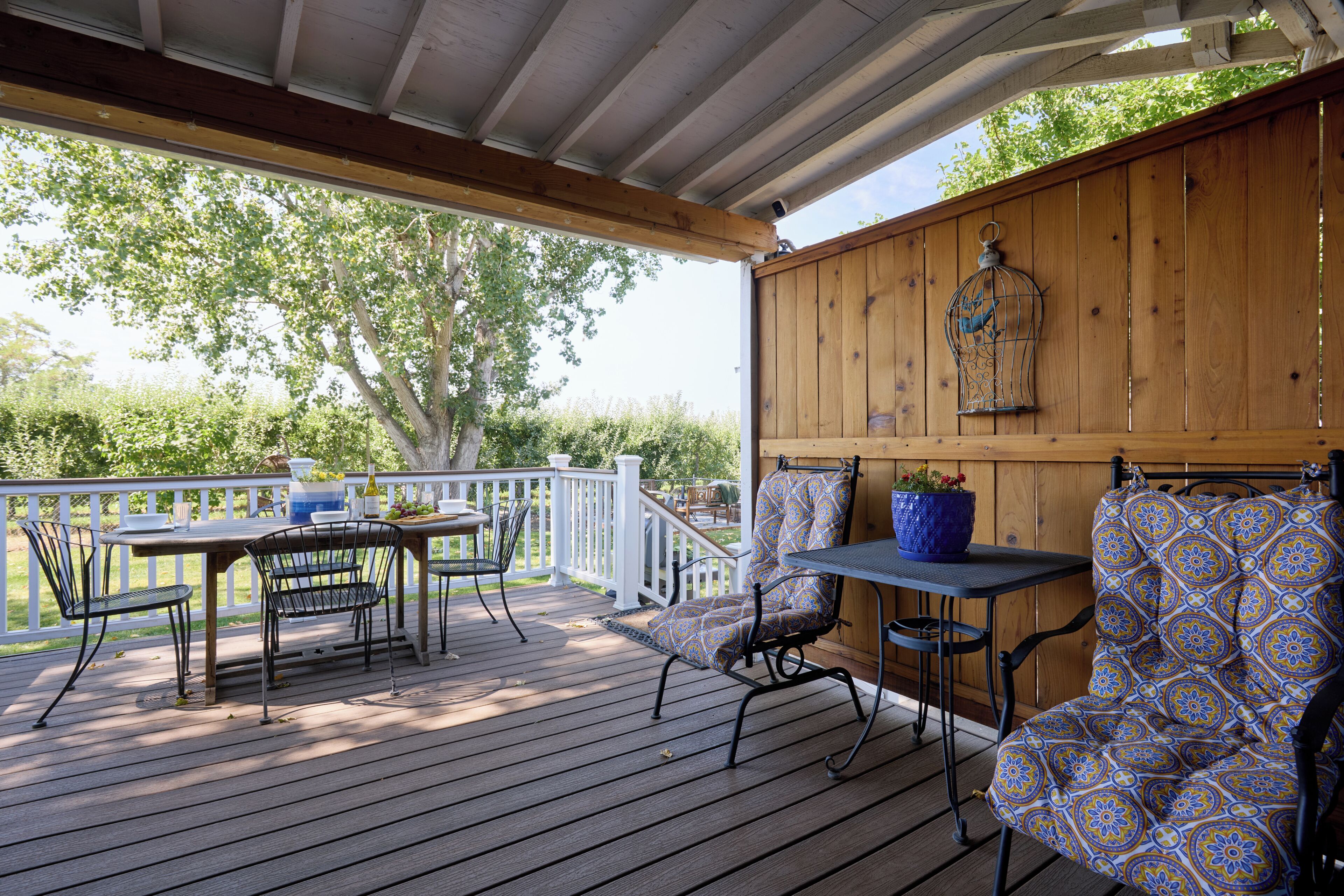 Una terraza techada al aire libre con mesa y sillas de madera, una jaula de pájaros y una planta en maceta.