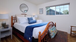 A neatly made bed with a wooden headboard, a bedside table with a lamp, and a window with a view of a house. - Sleep Inside Wine Country | 4BR, Fireplace (Milton-Freewater)
