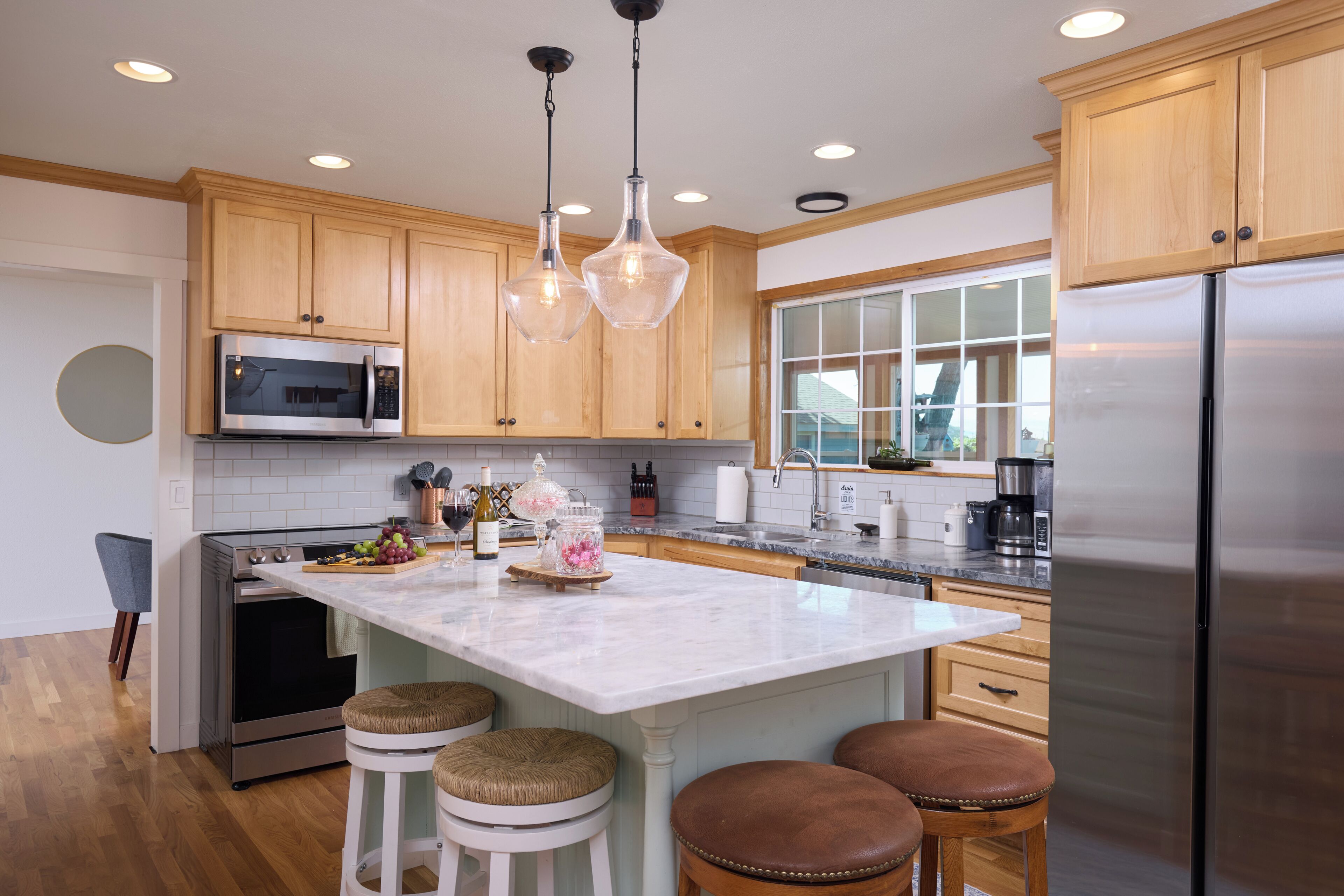 Una cocina moderna con armarios de madera, electrodomésticos de acero inoxidable, una isla de mármol e iluminación colgante.