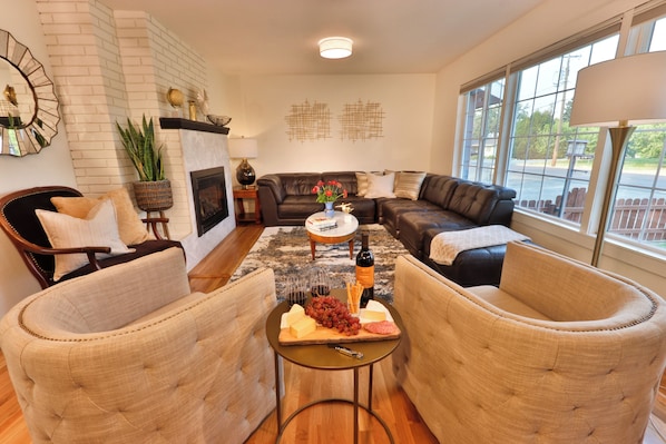 A living room with a fireplace, leather sofas, a coffee table with snacks, and a large window.
