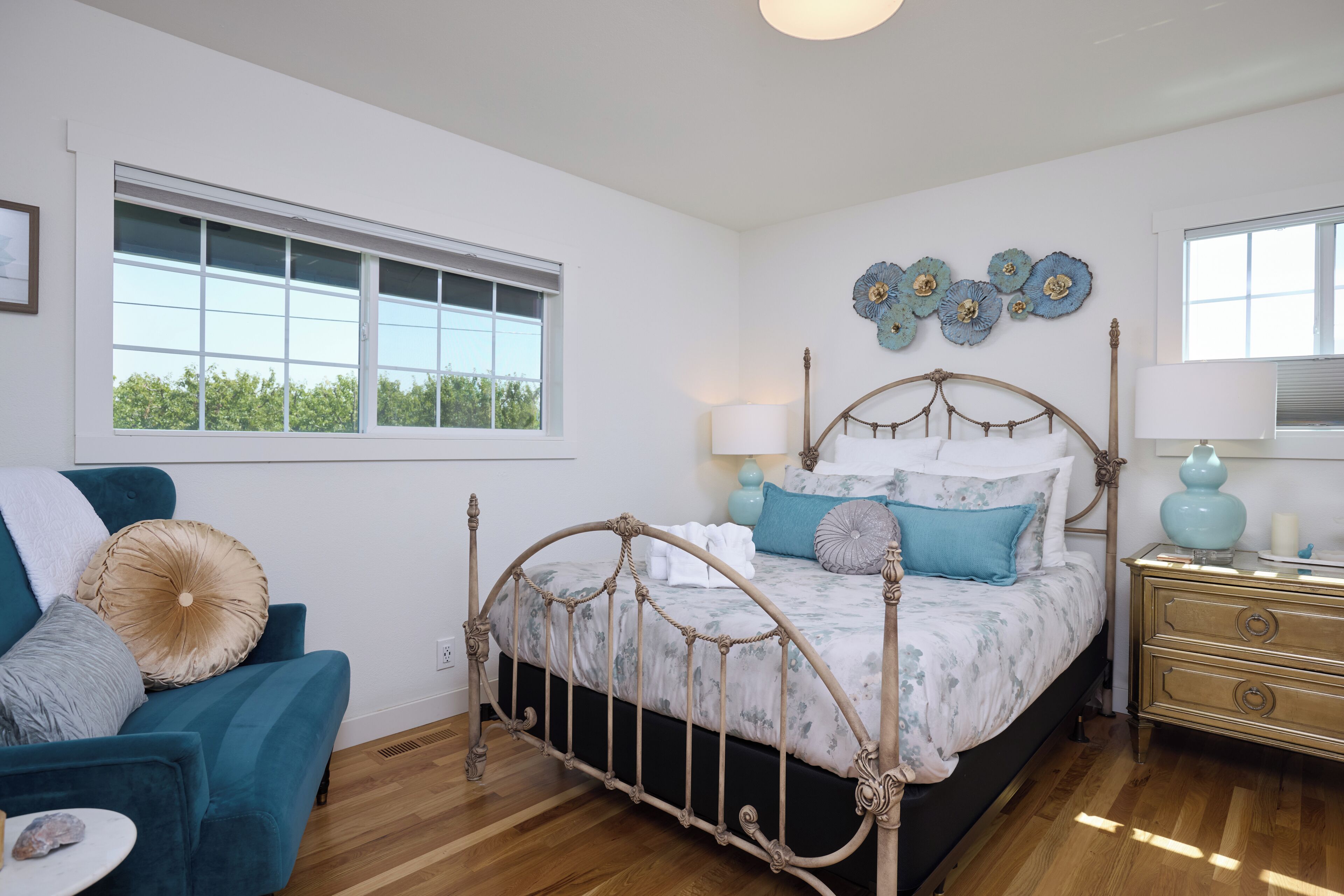 A bedroom with a four-poster bed, a nightstand, a chair, and a window with a view of trees.