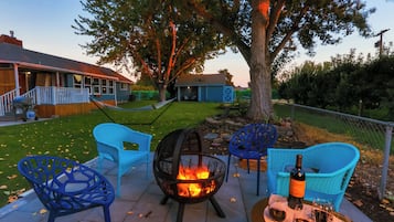 A patio with outdoor seating, a fire pit, and a table with a bottle and glasses.