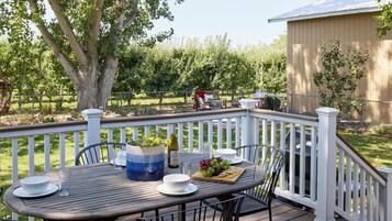 An outdoor deck with a table set for dining, surrounded by chairs, and a large tree in the background.