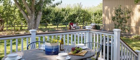 An outdoor deck with a table set for dining, surrounded by chairs, and a large tree in the background.
