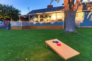 Une terrasse en bois avec une table et des chaises, un arbre et une maison en arrière-plan.