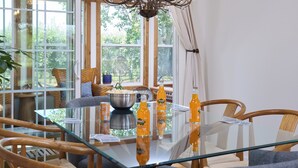 A dining area with a glass table, wooden chairs, a chandelier, and a view through large windows. - Sleep Inside Wine Country | 4BR, Fireplace (Milton-Freewater)