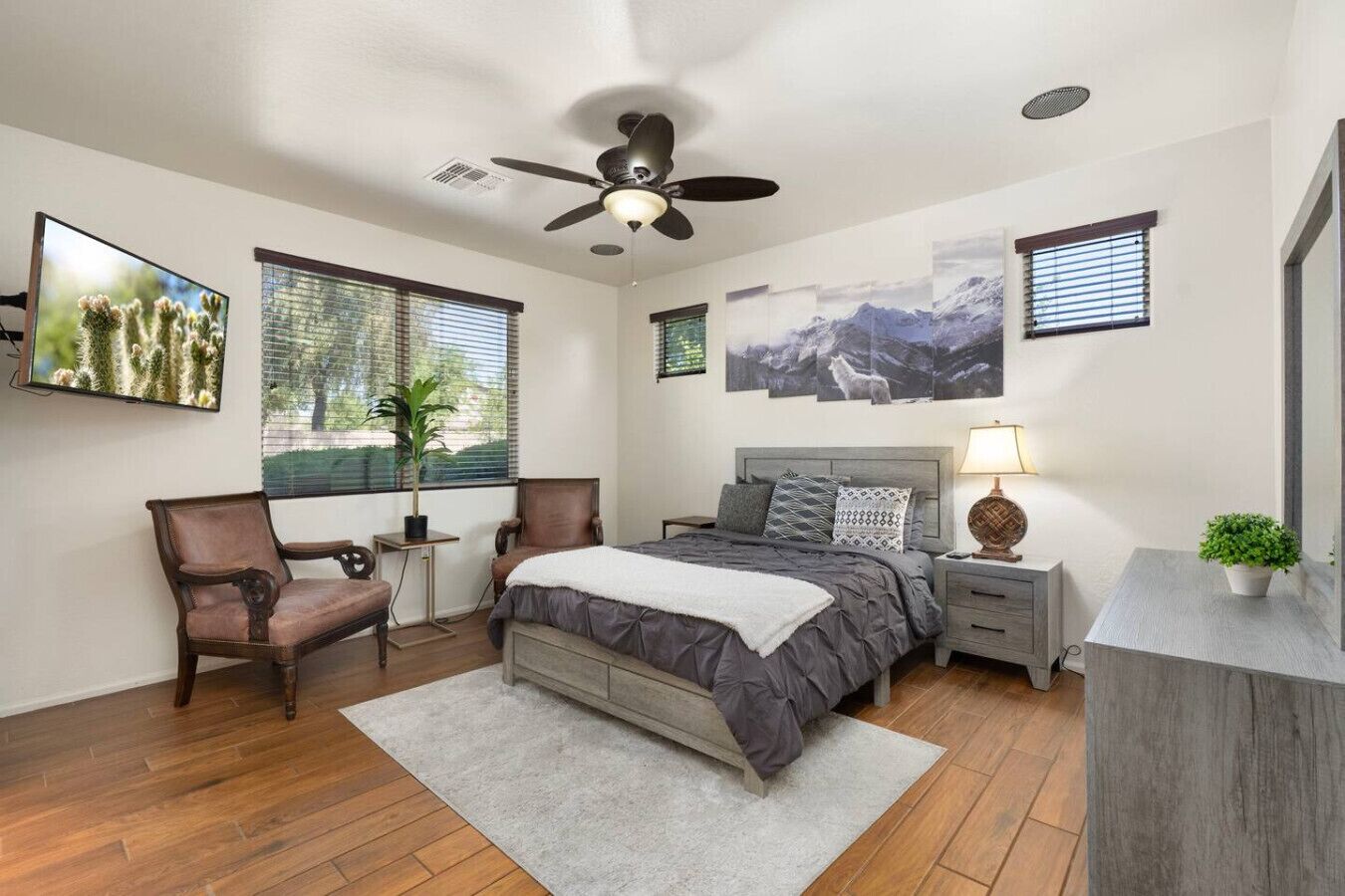 Une chambre à coucher comprenant un lit, un bureau, une chaise, un ventilateur de plafond et des œuvres d’art accrochées aux murs.