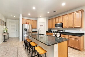 A modern kitchen with a central island, wooden cabinets, stainless steel appliances, and a bar stool seating area. - 5 Min to Stadium • Putting Green + BBQ (Glendale)