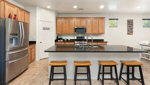 A modern kitchen with wooden cabinets, stainless steel appliances, a central island with stools, and a visible pantry door. - 5 Min to Stadium • Putting Green + BBQ (Glendale)