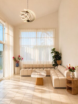 A modern living room with a sectional sofa, a round coffee table, and a hanging light fixture. - Sip, Swim, Repeat - 5BR Waterfront Pool Escape (Mermaid Waters)