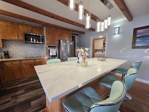 A kitchen with wooden cabinets, stainless steel appliances, a marble island, and teal chairs.