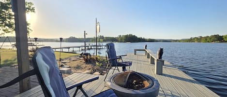 Une terrasse en bois avec des chaises longues et un foyer extérieur, le tout offrant une vue sur un lac.