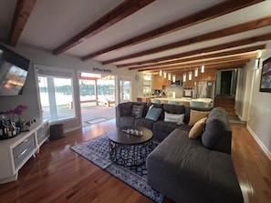 A modern living room with a sofa, coffee table, and a dining area with wooden beams and pendant lights.