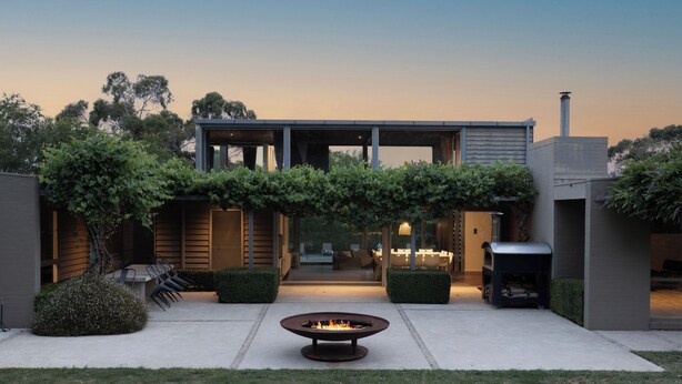A modern outdoor patio with a fire pit, seating, and a glass-enclosed dining area. - Thule Country Estate | Sleeps 12 | Private Lake, Pool & Farm | 45 mins Melbourne (Mount Macedon)