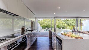 A modern kitchen with a large island, built-in appliances, and a view of a pool and greenery. - Thule Country Estate | Sleeps 12 | Private Lake, Pool & Farm | 45 mins Melbourne (Mount Macedon)