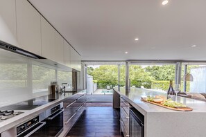 A modern kitchen with a large island, built-in appliances, and a view of a pool and greenery. - Thule Country Estate | Sleeps 12 | Private Lake, Pool & Farm | 45 mins Melbourne (Mount Macedon)