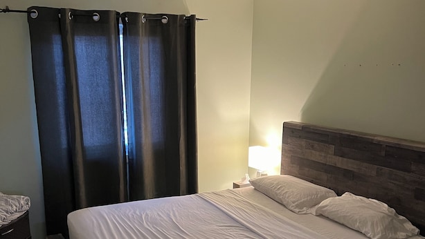 A bedroom with a bed, a nightstand, a lamp, and a ceiling light fixture. - Cozy Queen Room (Brampton)