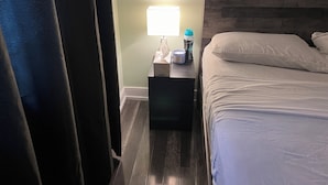 A hotel room with a bed, a nightstand with a lamp, a water bottle, and a tissue box. - Cozy Queen Room (Brampton)