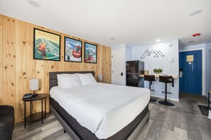 Ein Hotelzimmer mit einem Bett, einem kleinen Tisch mit einer Lampe, einem Kühlschrank und einer blauen Tür.