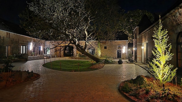A courtyard with brick buildings, a paved walkway, and illuminated trees. - Gîte with 9 rooms for 24 people (BRAINE LE COMTE)