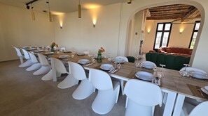 Une longue table à manger, entourée de chaises blanches, avec une table en bois et un canapé vert en arrière-plan.