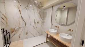 Un baño moderno con paredes de mármol, ducha, dos lavamanos y un espejo grande.