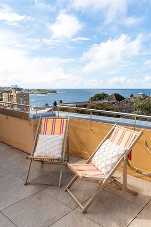 Two lounge chairs on a balcony with a view of the sea and buildings in the distance. - Art Deco Coogee Apartment | 5-Min Walk to Beach (Coogee)