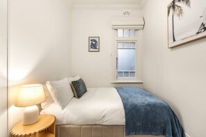 A bedroom with a bed, a bedside lamp, a window, and a wall-mounted picture. - Art Deco Coogee Apartment | 5-Min Walk to Beach (Coogee)