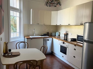 A compact kitchen with white cabinetry, a dishwasher, a stove, a microwave, and a refrigerator. - Art Deco Coastal Retreat, 250m to Coogee Beach (Coogee)