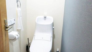 Um banheiro pequeno com vaso sanitário, bidê, porta-toalhas, rolo de papel higiênico e um par de chinelos sobre um tapete.