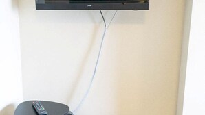 Televisão presa na parede, com um controle remoto sobre um banquinho.