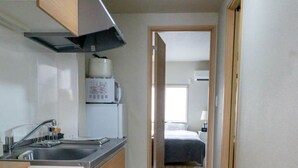 Um corredor estreito com uma cozinha de um lado, uma cama no outro e um par de sapatos no chão.