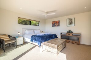 A bedroom with a bed, a nightstand, a chair, a wooden chest, and a ceiling fan. - Hekereua Heights - Spa & Ocean Views (Waiheke Island)