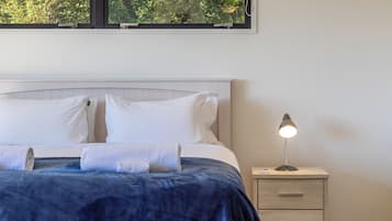 A neatly made bed with white pillows and a blue blanket, a bedside lamp, and a nightstand with drawers.