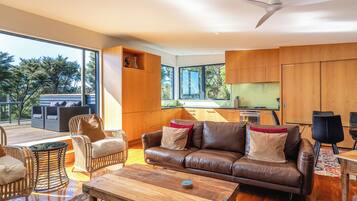 A modern living room with a leather sofa, wooden coffee table, wicker chairs, and a dining area.