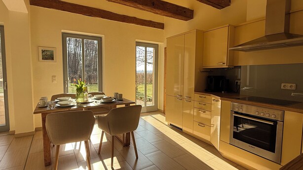 A modern kitchen with wooden beams, a dining area with chairs, and a view through large windows. - Stylishly furnished first floor apartment with garden view (Rheinsberg)
