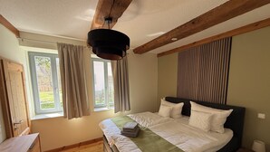 A bedroom with a bed, wooden floor, a window with curtains, a wooden dresser, and a ceiling light fixture. - Stylishly furnished first floor apartment with garden view (Rheinsberg)