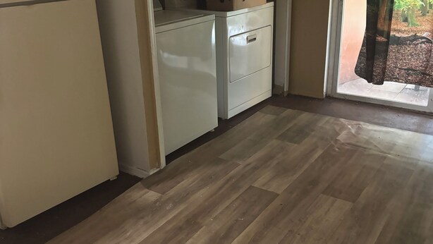 A compact kitchen with a refrigerator, a built-in oven, and a microwave. There is a small window with a curtain, and a door leading outside.