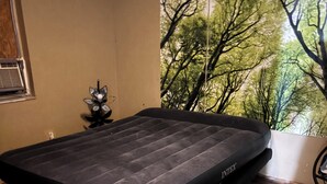 A room with a bed, a window with a view of trees, and a wall-mounted air conditioner.
