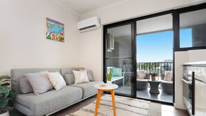 Un salon moderne avec un canapé gris, une petite table ronde et un balcon aménagé avec du mobilier d’extérieur.