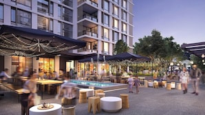 Un espace extérieur aménagé pour les repas, avec des tables et des parasols, une piscine, et un bâtiment doté de balcons en arrière-plan.