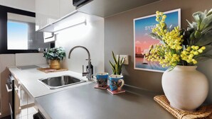 A modern kitchen with a stainless steel sink, a flat-screen TV mounted above the counter, and a framed picture of Sydney on the wall. - Beautiful Studio with City Views in Randwick (Randwick)