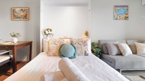 A bedroom with a bed, a sofa, a table, and two paintings on the walls. - Beautiful Studio with City Views in Randwick (Randwick)